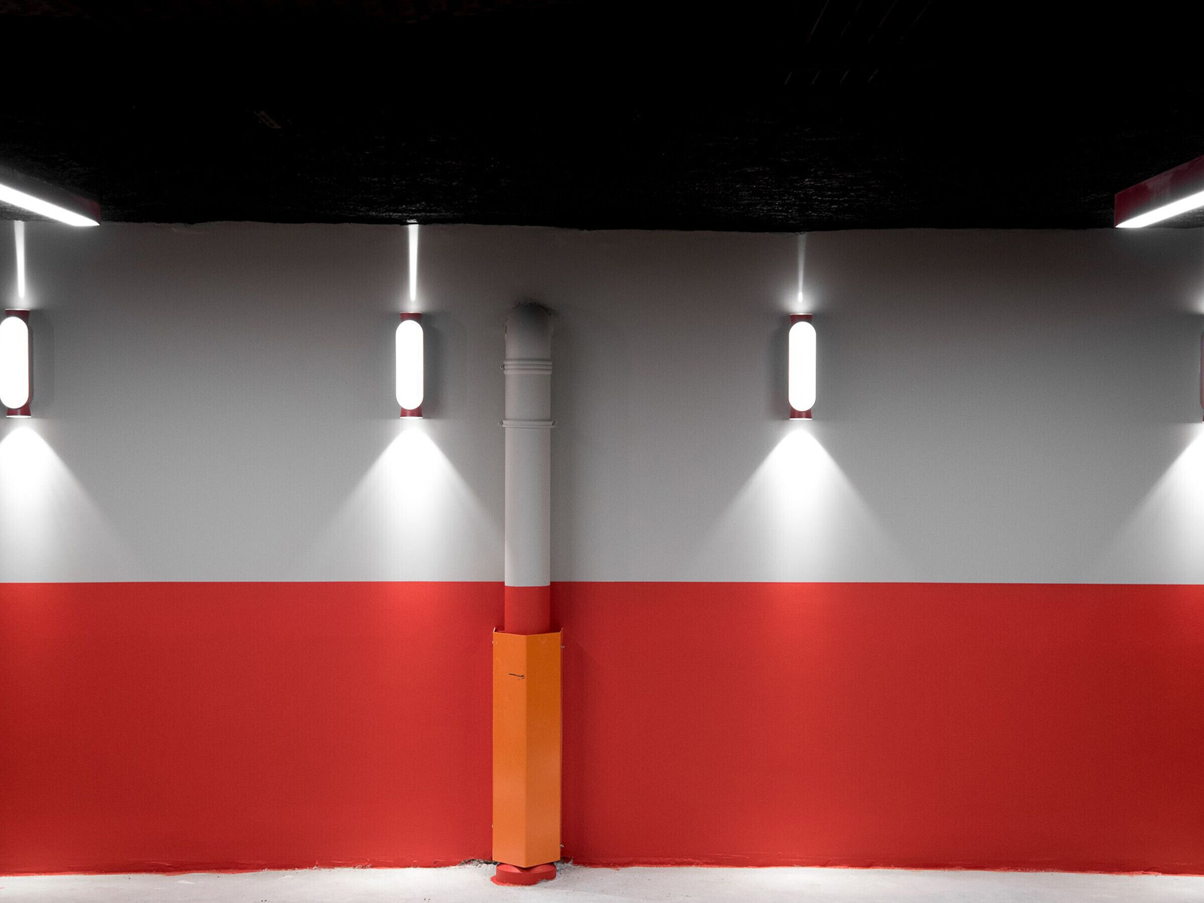 A corridor with a red and white wall, a central ventilation duct, and three wall-mounted lights.