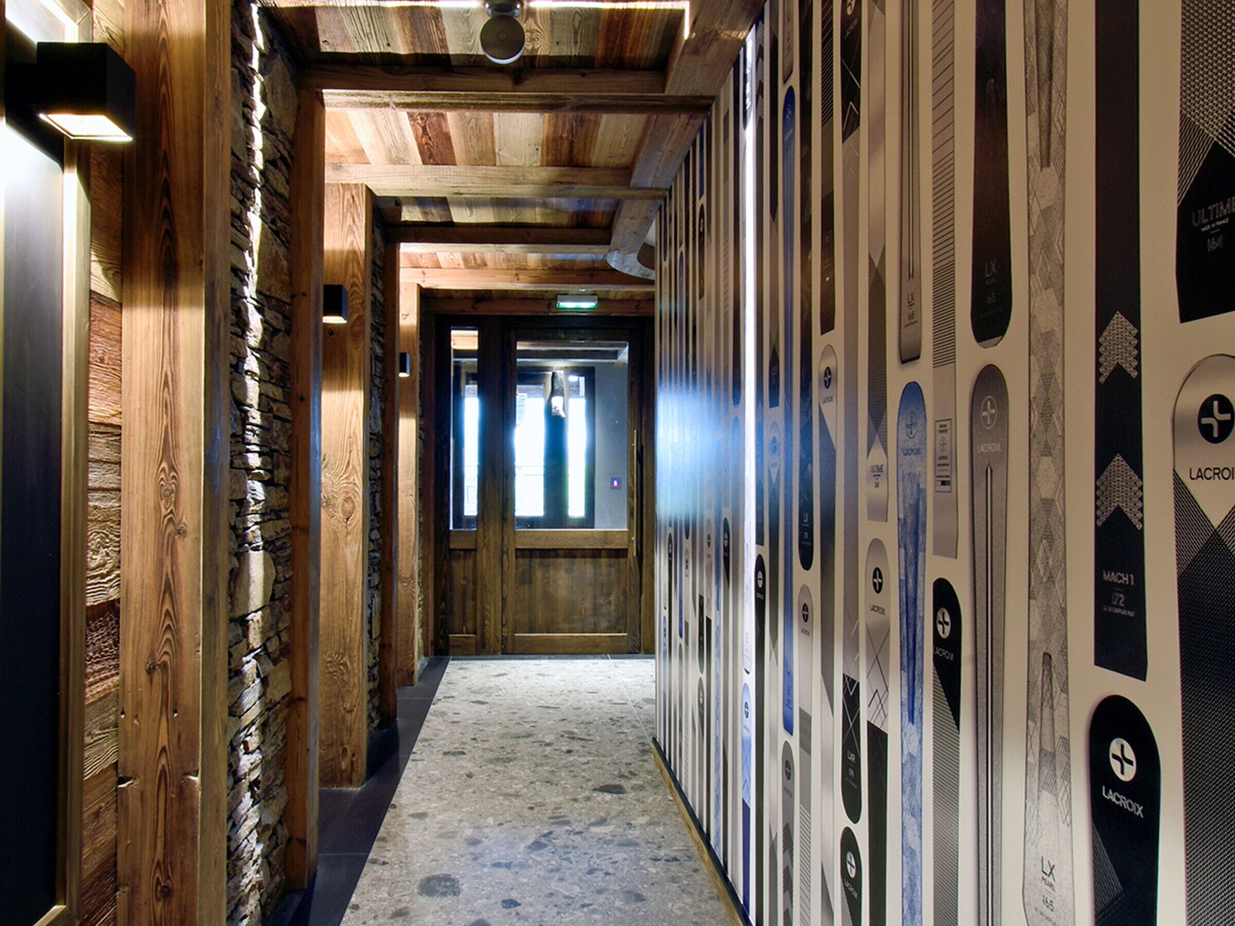Un couloir aux murs en bois et un mur d’accent en pierre, qui mène à une pièce dotée d’une grande fenêtre.