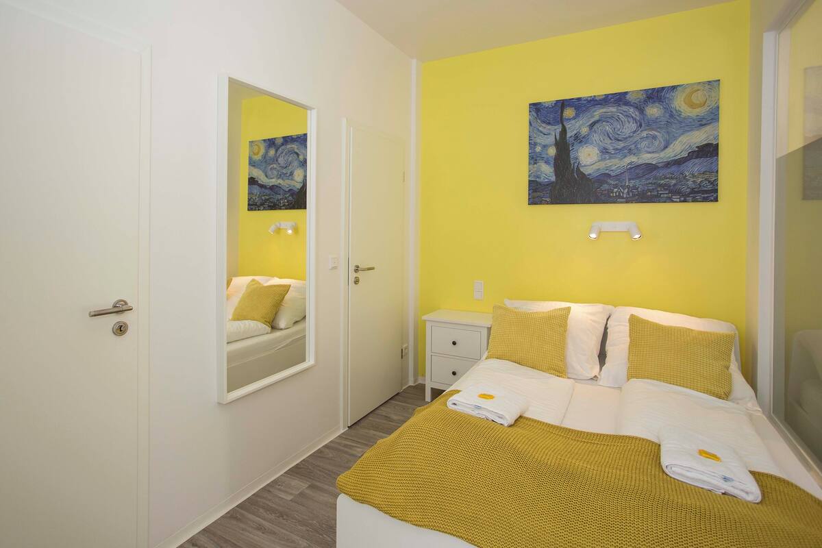Ein Zimmer mit Bett, Nachttisch, Spiegel und einem Bild an der Wand.