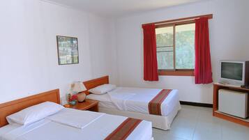 Habitación de hotel con dos camas individuales, televisión, una mesita con lámpara y ventana con cortinas rojas.
