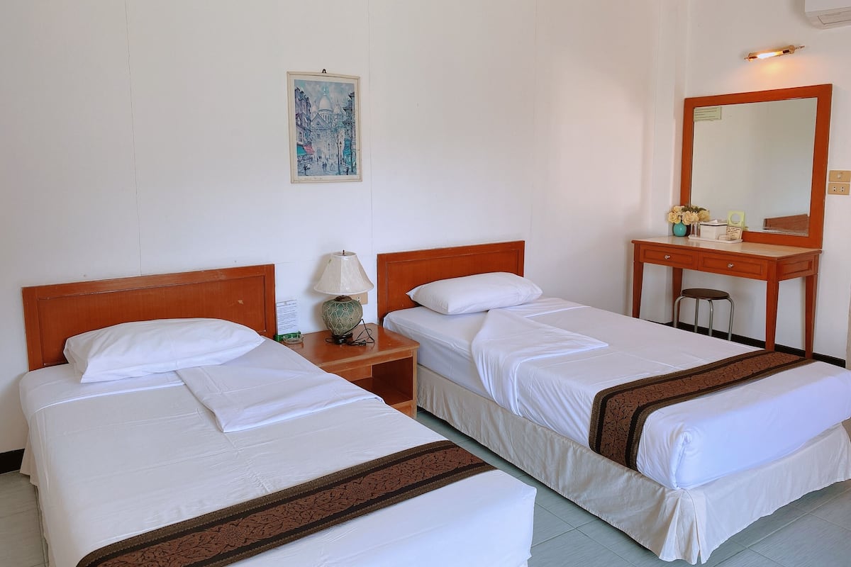 Ein Hotelzimmer mit zwei Einzelbetten, einem Nachttisch aus Holz mit Lampe, einem Schreibtisch mit Spiegel und einem gerahmten Bild an der Wand.
