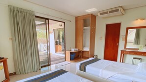 Ein Hotelzimmer mit zwei Betten, einem Holztisch, einem Spiegel und einer Schiebetür aus Glas, die zu einem Außenbereich führt.