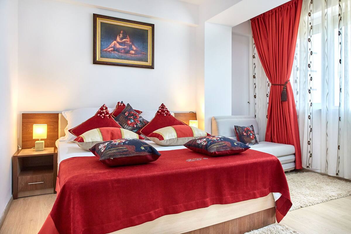 Une chambre bien rangée, avec un lit, une table de chevet, un canapé et une fenêtre avec des rideaux.
