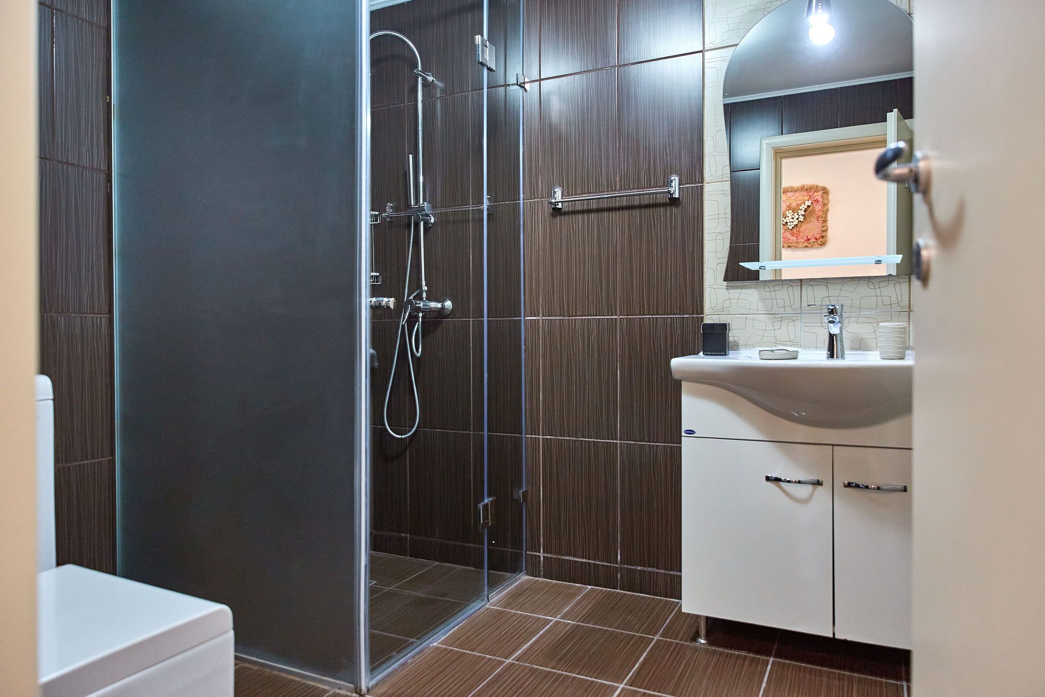 Une salle de bain moderne avec une douche en verre, un lavabo blanc et un miroir agrémenté d’un élément décoratif.