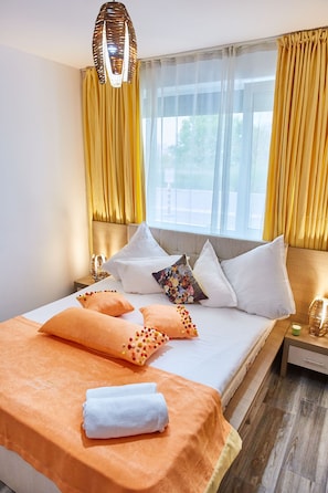 Una cama bien hecha con una colcha blanca y naranja, varios almohadones y una lámpara colgante decorativa.