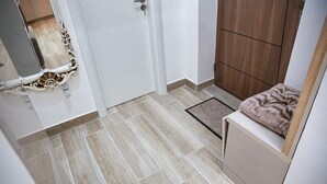 A bathroom with a tiled floor, a white door, a wooden cabinet, and a mirror with ornate detailing. - Fairy Tale 1 BDR Apartment in City Center (Žabljak)
