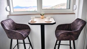 A small table with two chairs and a vase of flowers, positioned near a window with a view of a landscape. - Fairy Tale 1 BDR Apartment in City Center (Žabljak)