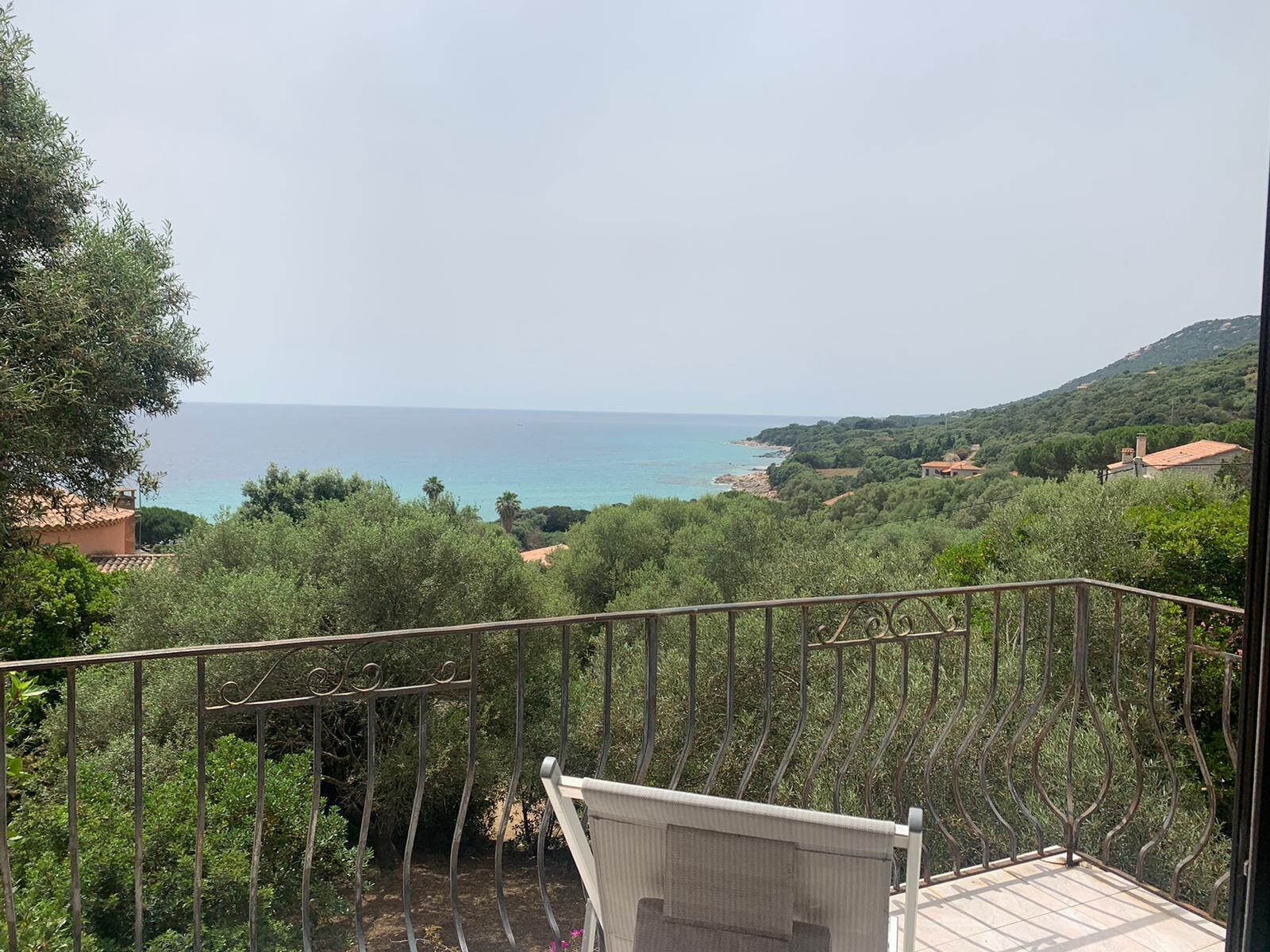 A balcony with a view of the sea and surrounding greenery.