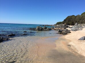 Ein Strand mit klarem, flachem Wasser, Felsformationen und einem Sandufer.