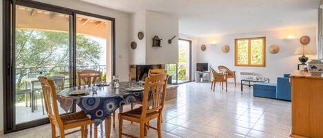 A spacious dining area with a large table and chairs, a kitchen in the background, and a balcony with outdoor seating.