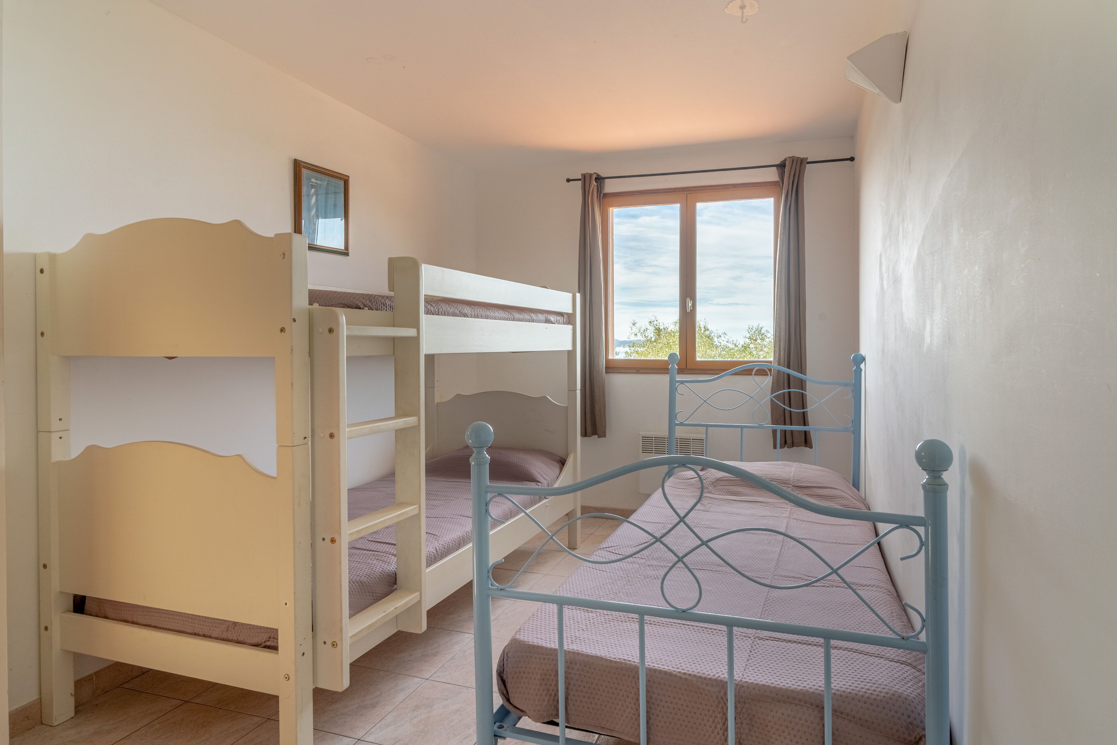 Quarto com beliches, janela com cortinas e vista para árvores.