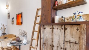 Un intérieur rustique avec une échelle en bois, une table en verre ornée d’un vase, des meubles en osier et une étagère contenant des ustensiles de cuisine.