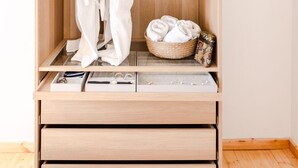 Une armoire en bois avec une tringle pour suspendre les vêtements, un panier contenant des serviettes pliées et une boîte à bijoux.