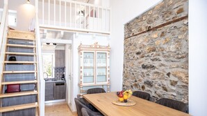 Un coin repas avec une table et des chaises en bois, un panier de fruits et un mur en pierre.
