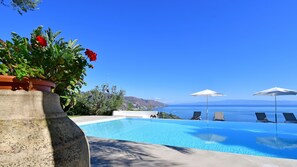 A swimming pool with lounge chairs and umbrellas, a view of the sea, and a potted plant with red flowers. - Villa Karin 7 in Taormina (Taormina)