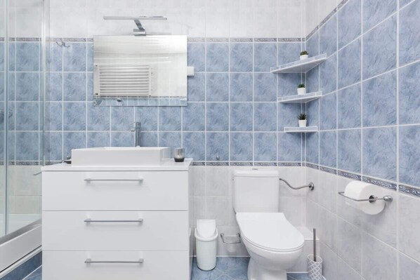 A bathroom with a white sink, toilet, and a mirror above the sink. There are shelves with plants on the wall. - Warsaw | Aleja Dwudziestolatków 3 | Two-level Apartment | Balcony (Warszawa)
