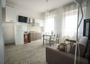 A modern kitchen with a flat-screen TV, a dining area with a table and chairs, and a living room with a sofa.