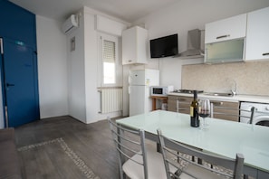 A modern kitchen with a dining table, chairs, a TV, and a blue door.