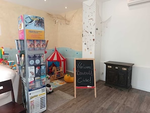 A room with a children's play area, a chalkboard with 'Welcome' written on it, and a small wooden cabinet.