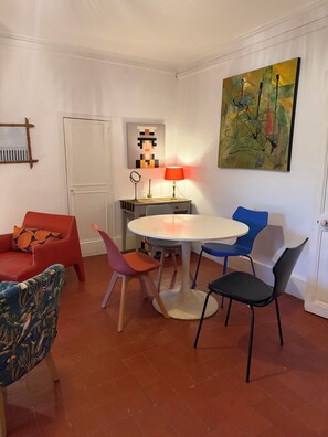 A room with a round table, chairs, a red sofa, a blue chair, and a painting on the wall.
