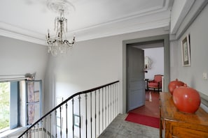 A staircase with a chandelier, a red carpet, and a wooden table with red objects. - Apartment 1 in a 2-star-rated writer's house (Sommières)