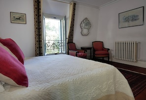 A hotel room with a large bed, a small table, two chairs, a radiator, and a window with curtains.