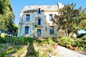 Ein großes, historisches Gebäude mit zahlreichen Fenstern und einem Balkon, umgeben von üppigen Gärten und Bäumen.