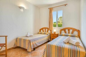 Une chambre avec deux lits, chacun doté de draps à rayures, une petite table, une lampe et une fenêtre avec un rideau.
