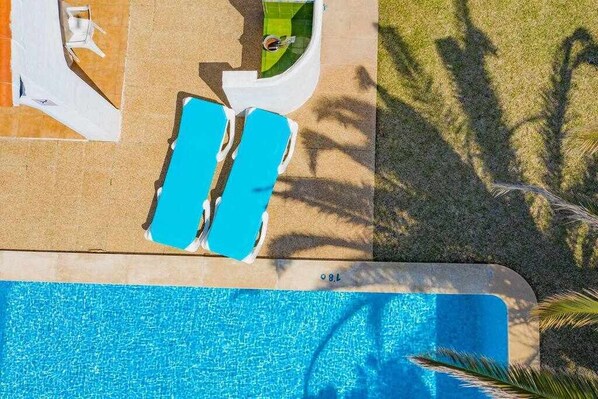 Vista aérea de uma área de piscina com duas espreguiçadeiras azuis e uma piscina pequena.