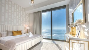 A modern bedroom with a large bed, a nightstand, a desk with a vase, and a view of the ocean. - Maison Privee - 5242 Emaar (Dubai)