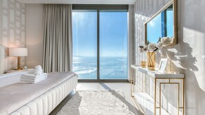 A modern bedroom with a large window, a bed, a bedside table with a lamp, and a mirror. - Maison Privee - 5242 Emaar (Dubai)