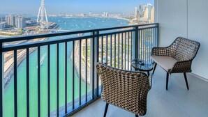 A balcony with wicker chairs and a small table, overlooking a marina with boats and a city skyline. - Maison Privee - 5242 Emaar (Dubai)