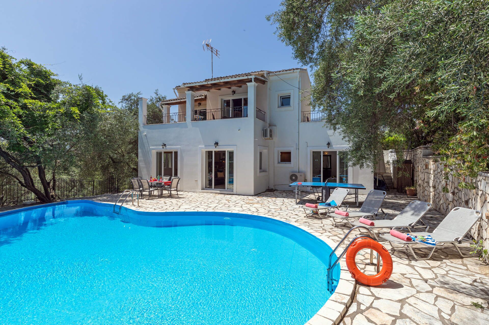 A two-story building with a swimming pool, outdoor seating, and a stone wall.