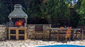 Een terras buiten met een stenen zwembad, een barbecue en een eettafel met stoelen.