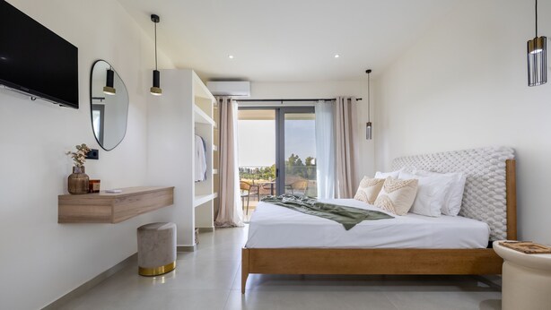 A modern bedroom with a large bed, a TV mounted on the wall, and a balcony with a view. - Kamara Apartments (Zakynthos)
