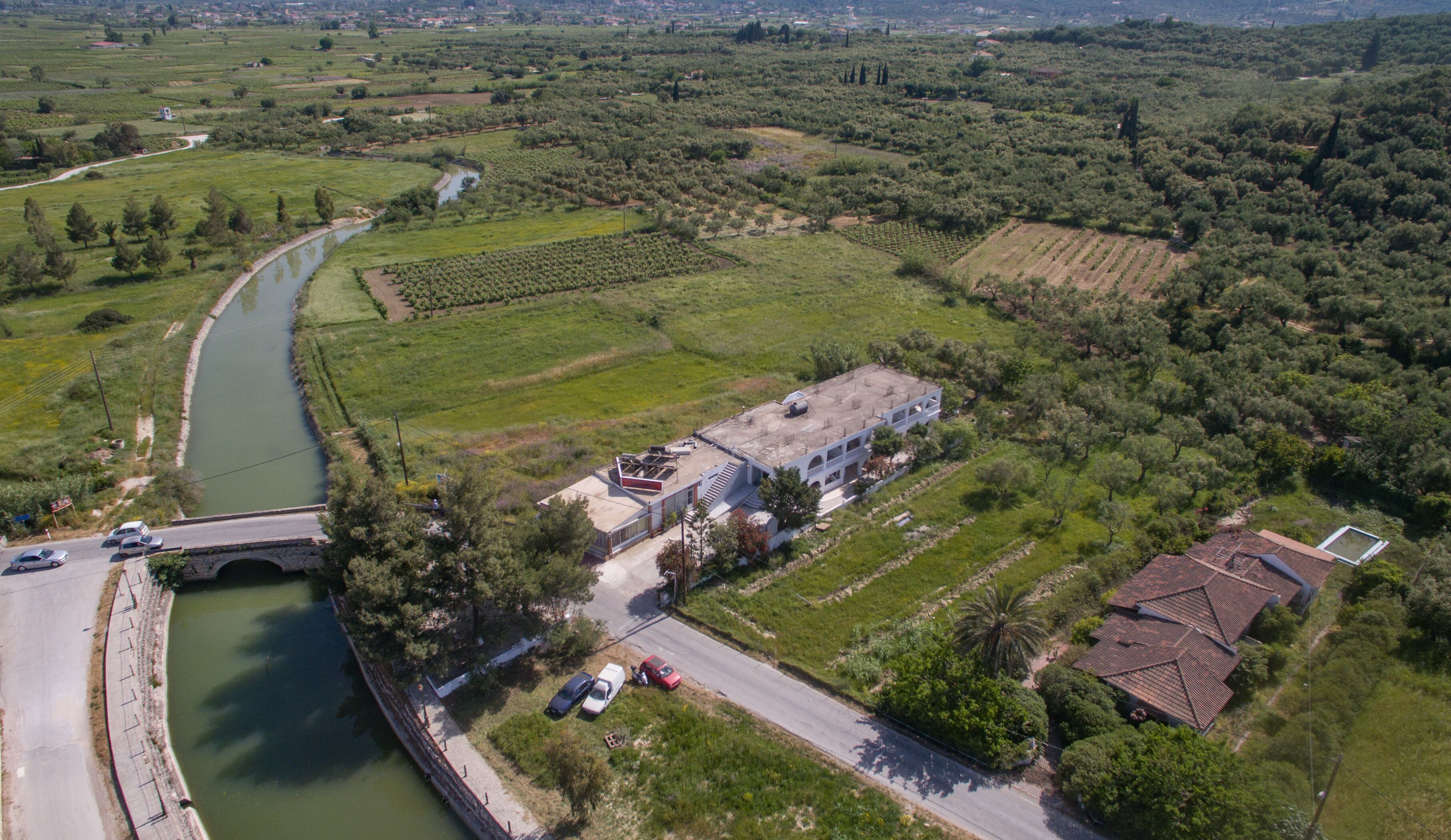 An aerial view of a rural area with a river, fields, and a building with a flat roof.
