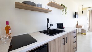 A modern kitchen with a black sink, wooden cabinets, and a countertop. There are shelves above the sink holding kitchen items. - Kamara Apartments (Zakynthos)