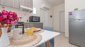 A modern kitchen with a refrigerator, microwave, and dining table set with a coffee mug, a glass of orange juice, and a plate of food. - Kamara Apartments (Zakynthos)