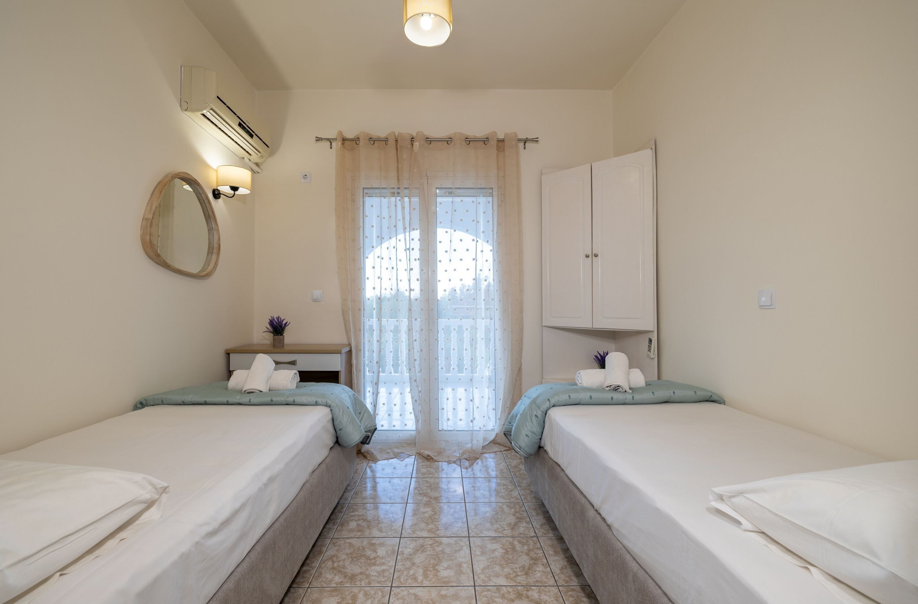 A hotel room with two single beds, a small desk with a lamp, a mirror, and a wardrobe.