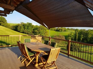 A wooden deck with a table and chairs, overlooking a green landscape.