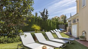 Un jardín con cuatro sillones de descanso, un árbol pequeño y un edificio al fondo.