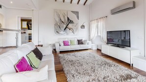 Una sala de estar moderna con un sofá blanco, un cuadro abstracto de gran tamaño, un televisor de pantalla plana y una alfombra mullida.