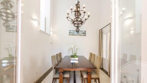 Un comedor con una mesa de madera, seis sillas, una lámpara de araña y un cuadro en la pared.