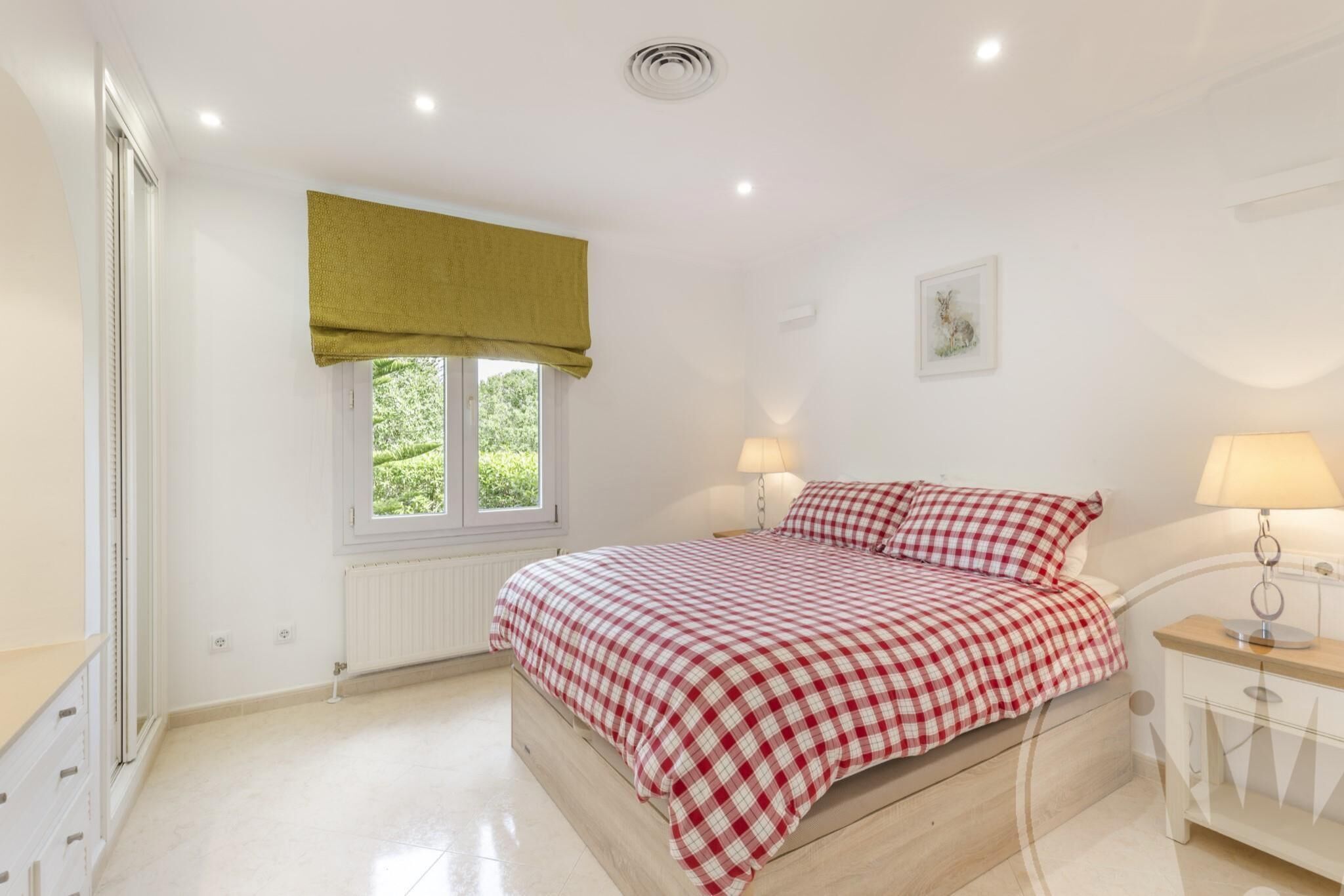 Un dormitorio con cama, lámparas de noche, una ventana con cortina verde y un radiador.