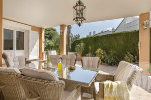Un patio exterior con mobiliario de mimbre, una mesa de vidrio y un farol.