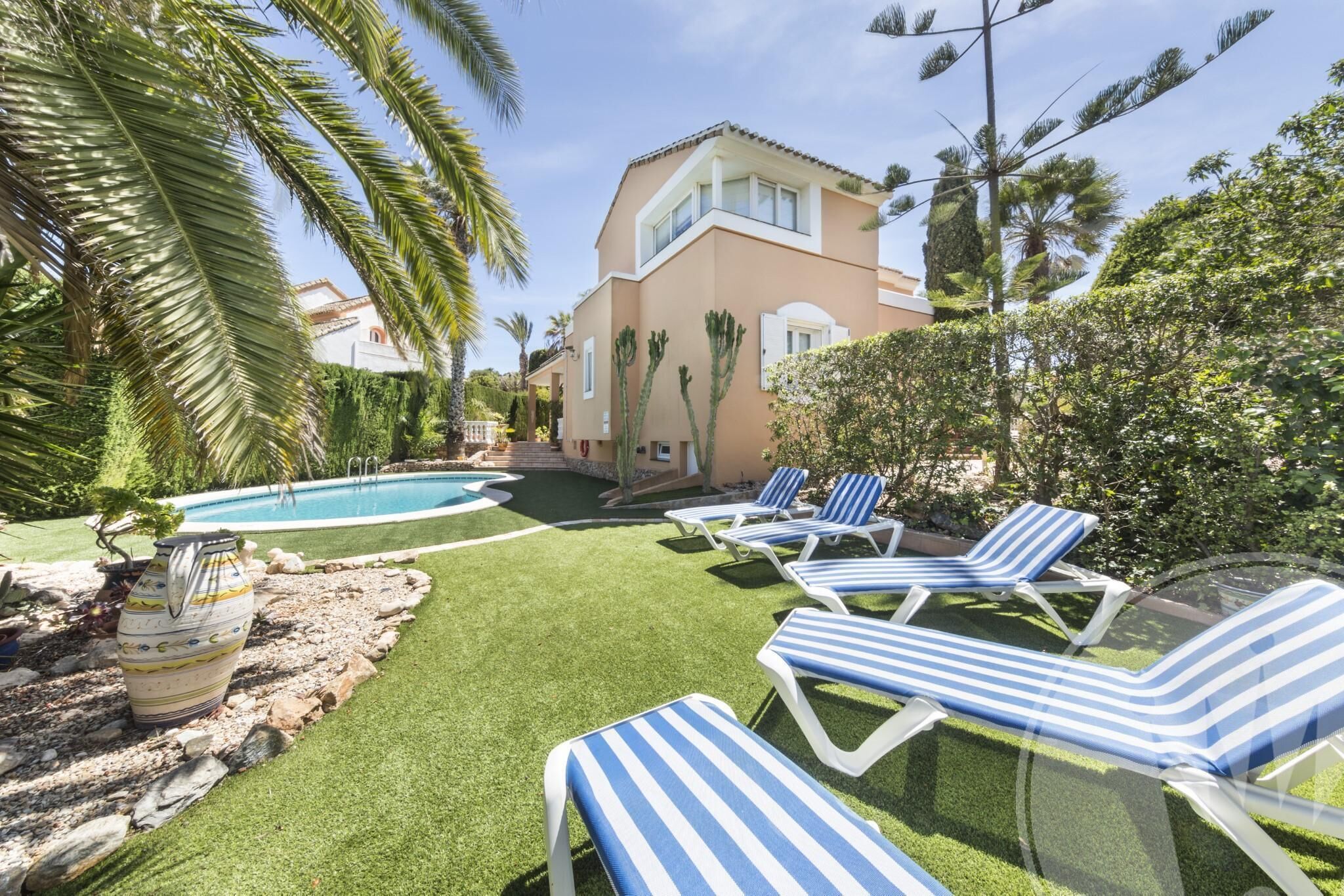 Un espace piscine avec une pelouse artificielle, des chaises longues et un bâtiment doté d’un balcon.