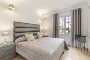 Une chambre moderne avec un grand lit, des lampes de chevet, un bureau avec une chaise et une fenêtre avec des rideaux.