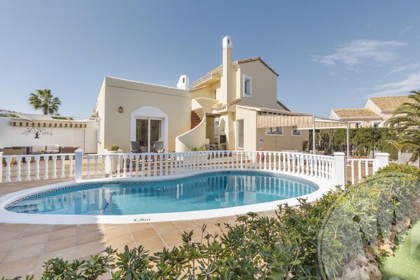 Un espace aménagé au bord d’une piscine, avec une piscine, une clôture blanche et un bâtiment doté d’un toit en tuiles.
