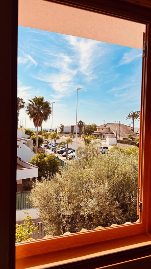 A view through a window of a residential area with parked cars, palm trees, and houses. - Sun and Sea (Sagunto)