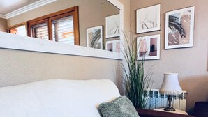 A bedroom with a bed, pillows, a nightstand, a lamp, a mirror, and framed pictures on the wall.